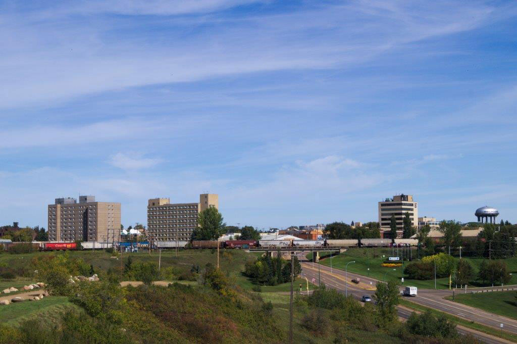 A clear blue sky, a series of large office buildings and a water tower separated by a stretch of highway