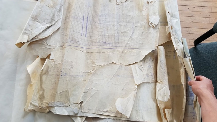 A person unrolls faded and torn large-scale paper maps.
