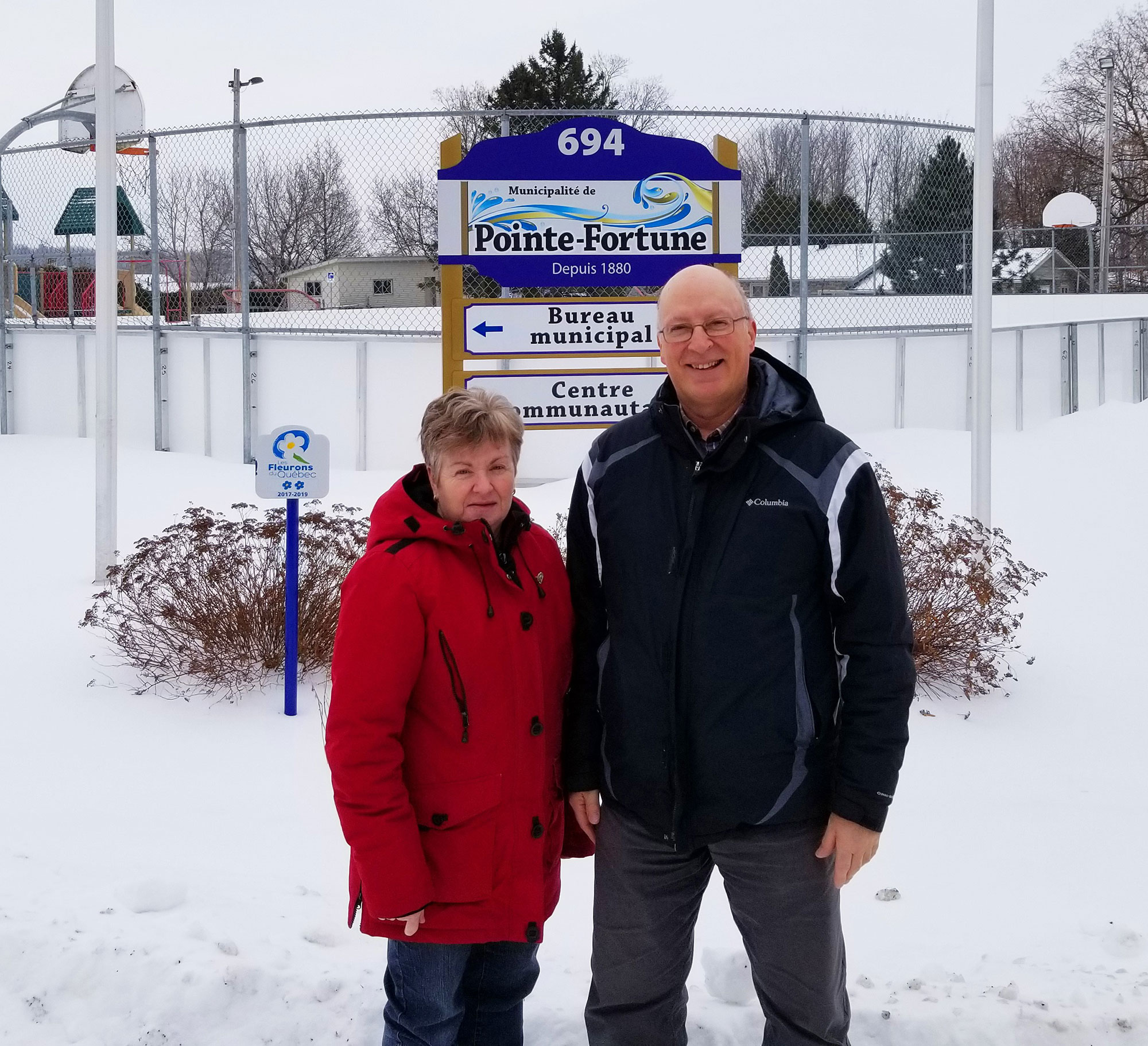 Un homme et une femme devant le panneau de la Ville de Pointe-Fortune et la patinoire extérieure.