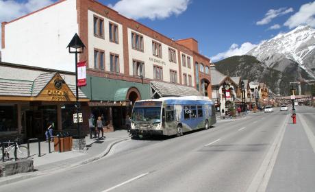 A hybrid bus waits for a pedestrian to cross in downtown Banff.