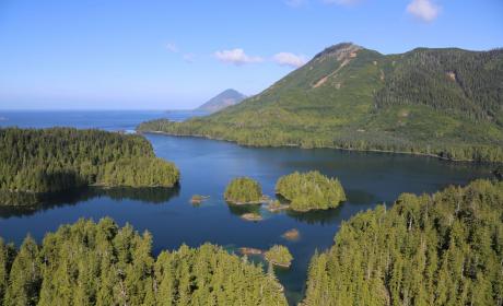 Aerial view of a river with several islands leading into a bay, surrounding by hills and conifer trees